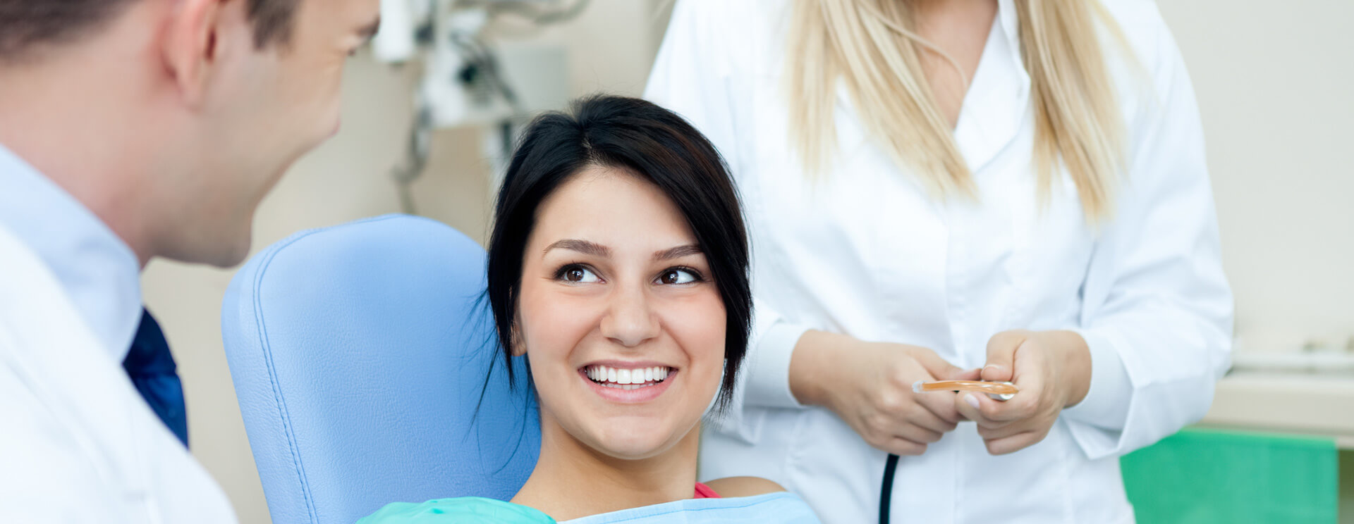 Female patient smiling while talking with dentist and assistant standing beghind